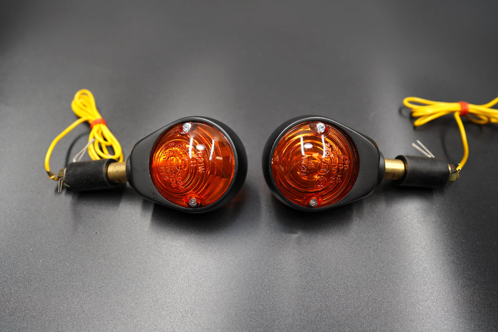 Front view of bar end turn signals with amber glass lens and matte black housing — vintage style motorcycle indicators.
