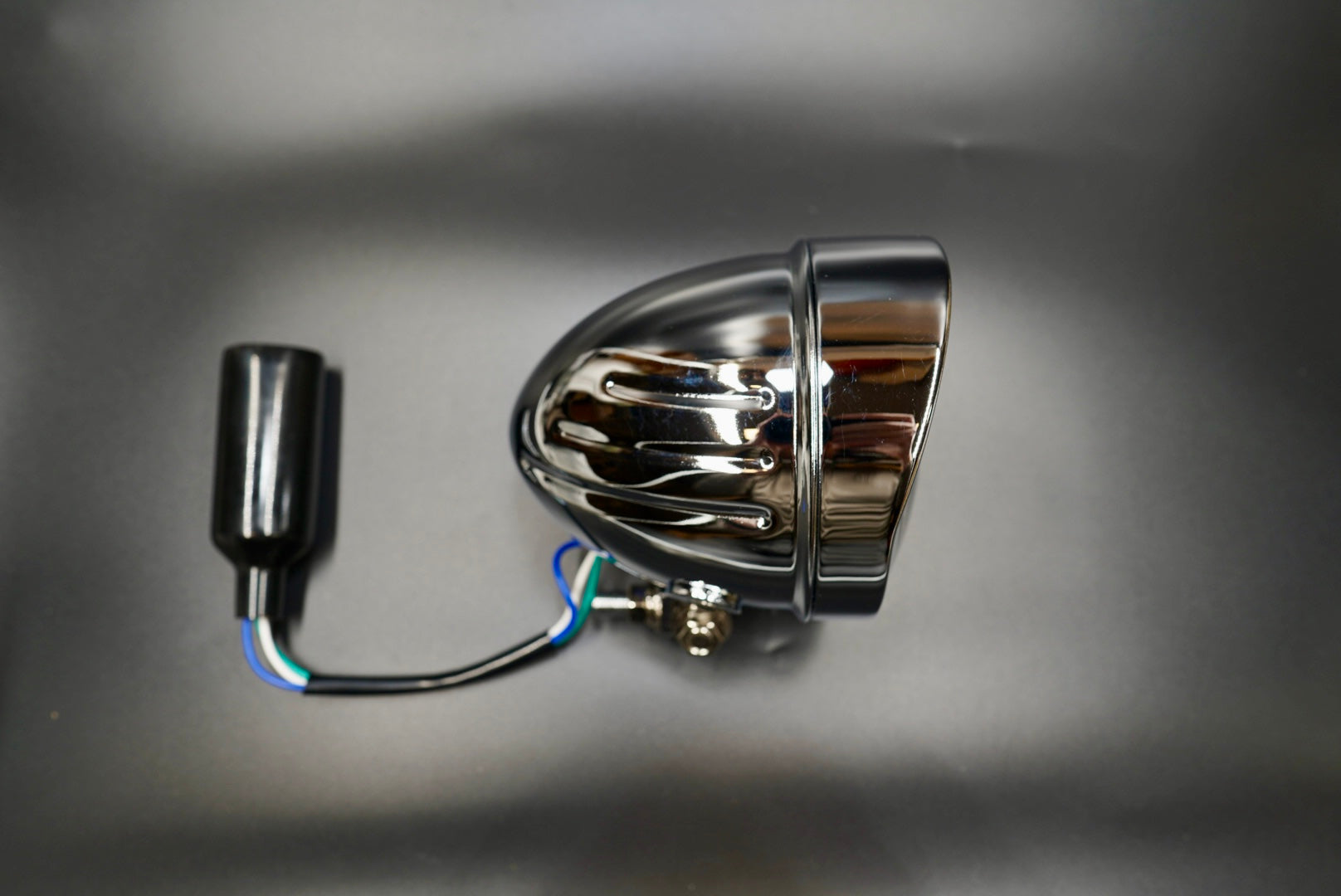 Side front view of Fin-Back classic motorcycle headlight with chrome shell and clear lens — vintage engineering design.