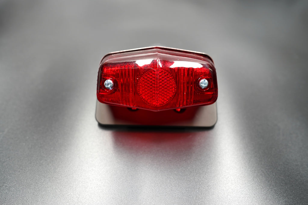 Front main view of Lucas 564-style vintage tail light — red lens with matte black body and polished trim.