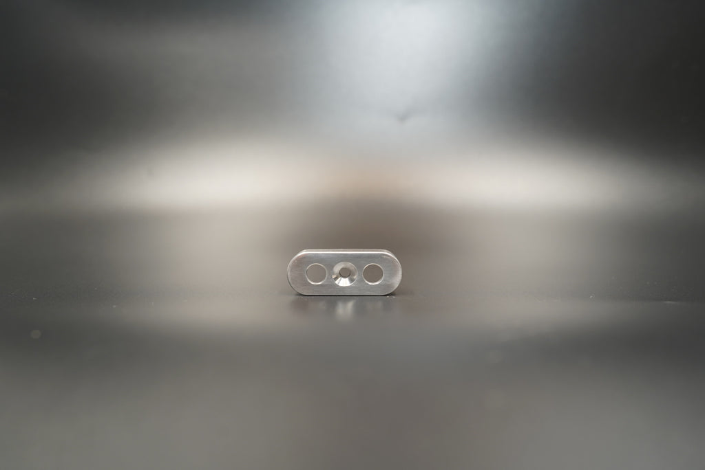 Dual-hole handlebar switch mount in raw silver finish on matte surface