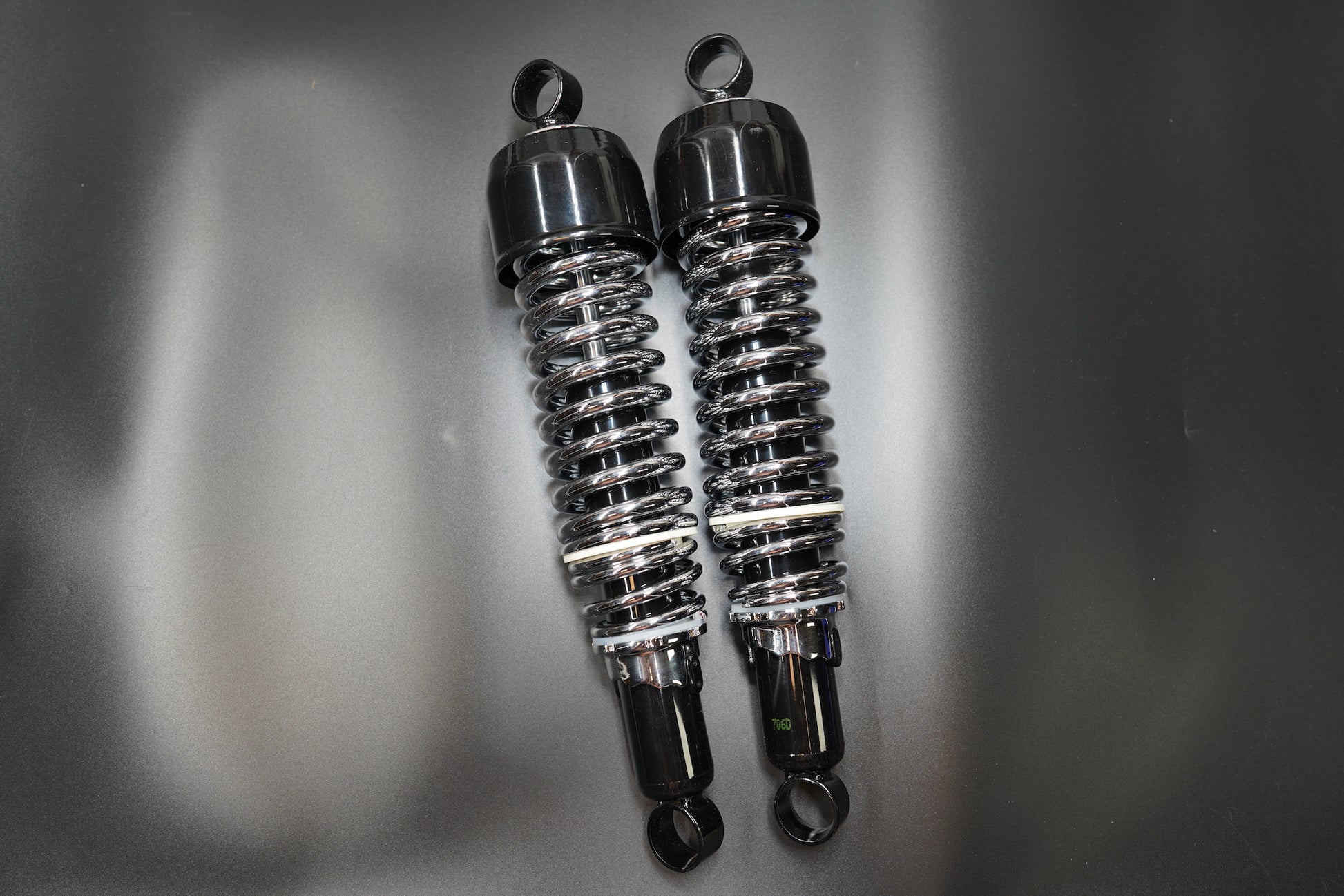 Side view of twin motorcycle shocks showing coiled spring detail and steel mounting eyes.