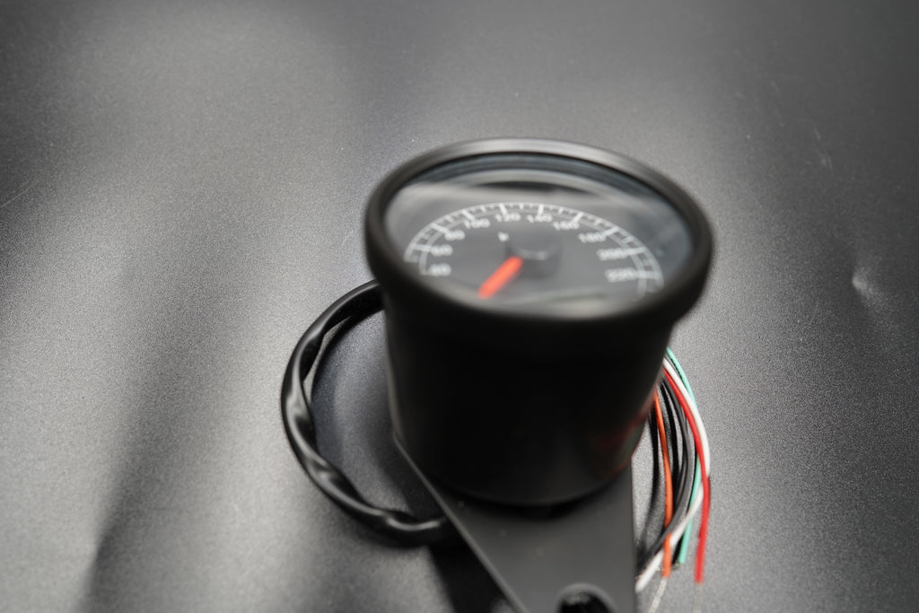 Side angle of 60mm speedometer showing curved glass face and wiring tail.