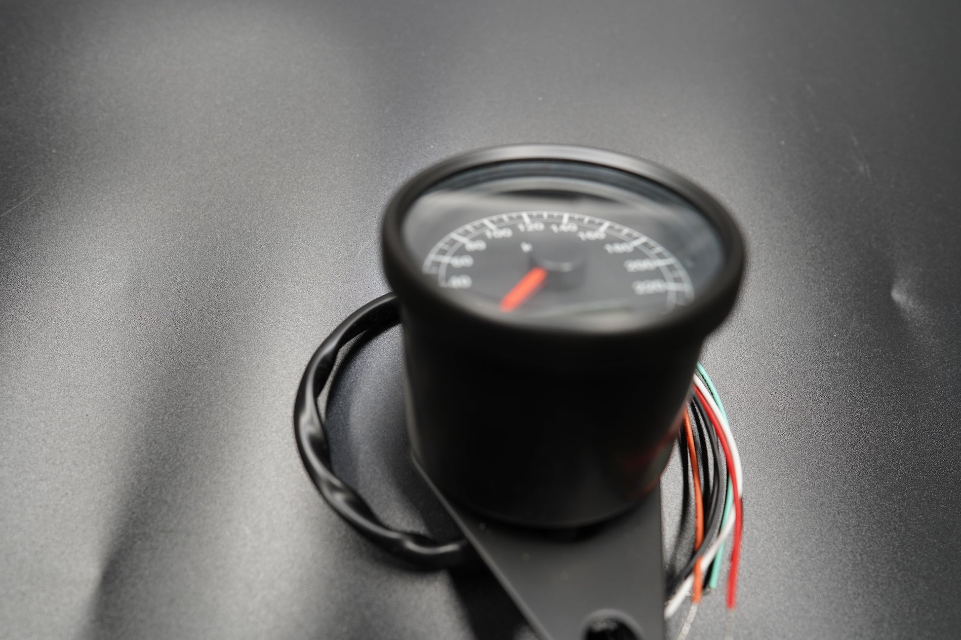 Side angle of 60mm speedometer showing curved glass face and wiring tail.