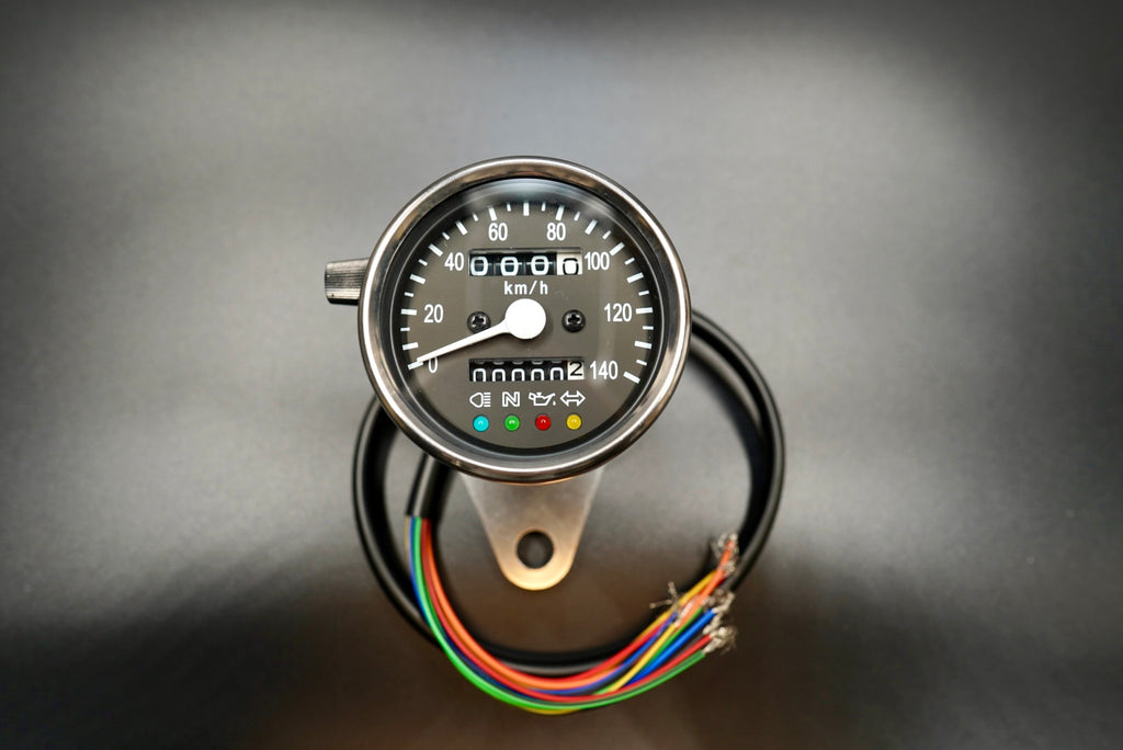 Black dial analog speedometer angled view showing wiring and indicator lights.