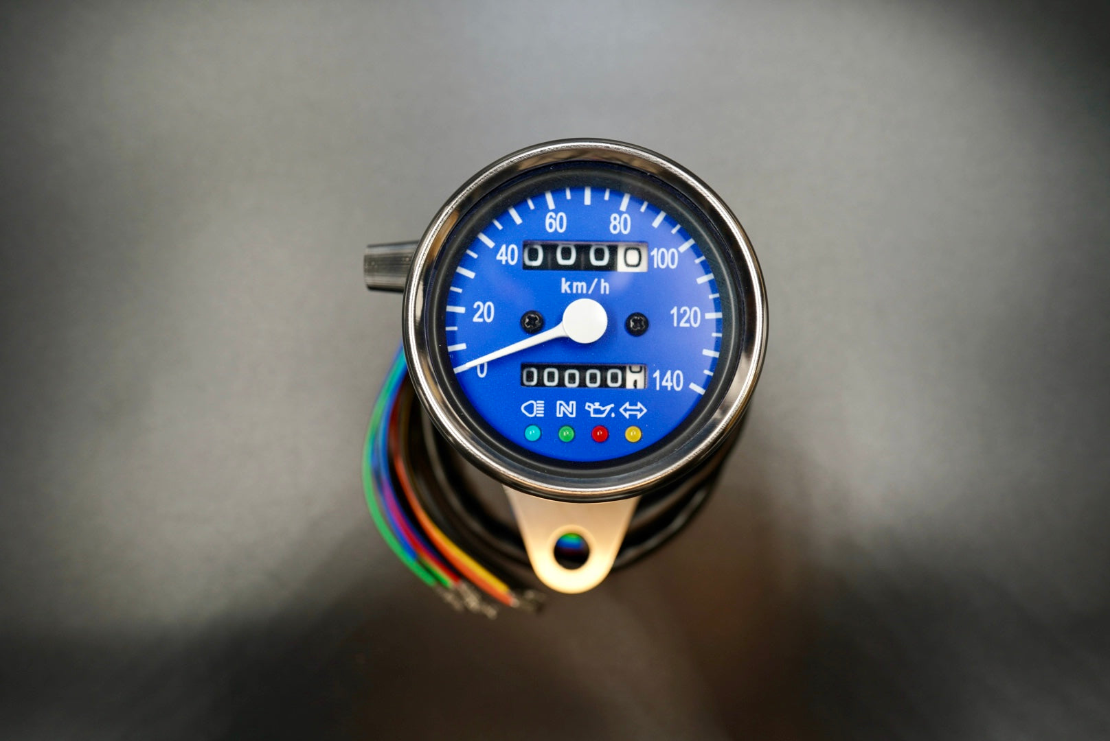 Blue dial version of the retro analog motorcycle speedometer with polished metal casing.