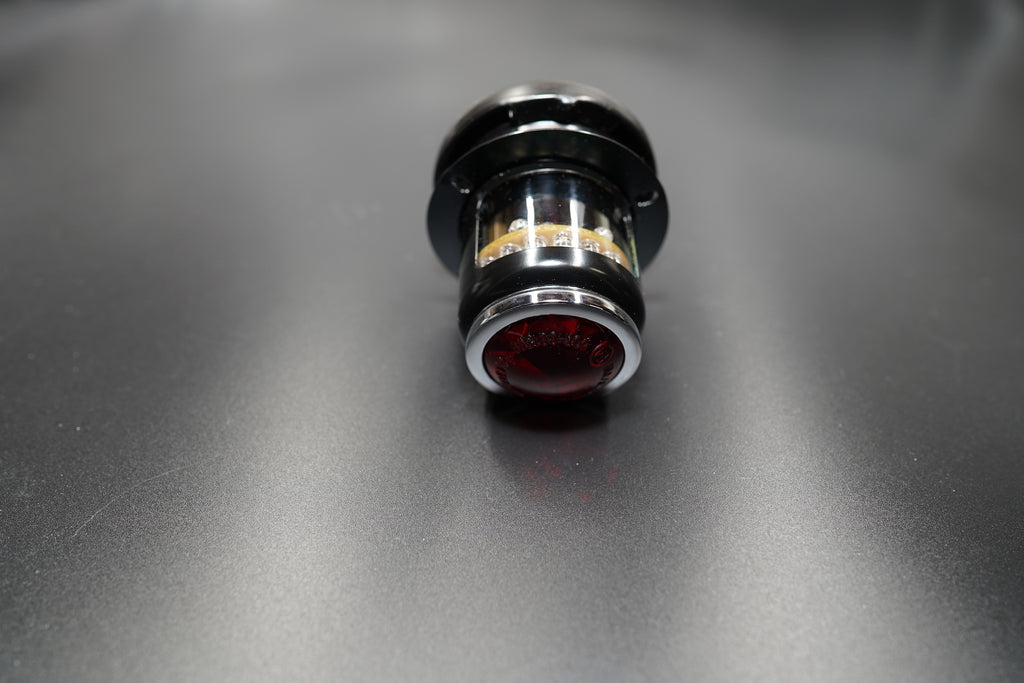 Front-centered view of 3-in-1 motorcycle tail light with red glass lens and matte black steel housing.