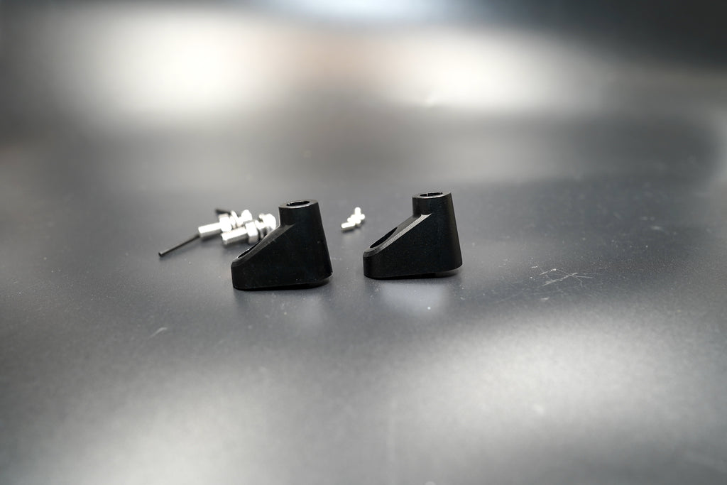 Pair of black anodized aluminum turn signal spacers with mounting bolts on metallic surface