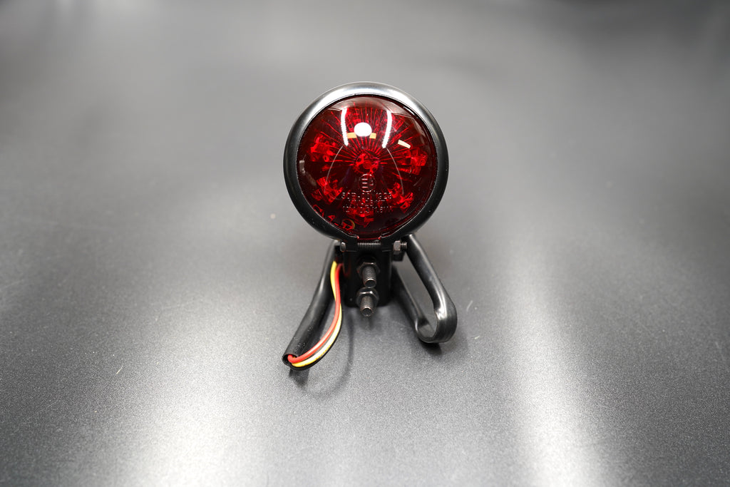 Front main view of vintage-style round LED tail light — domed red lens with matte black metal housing.