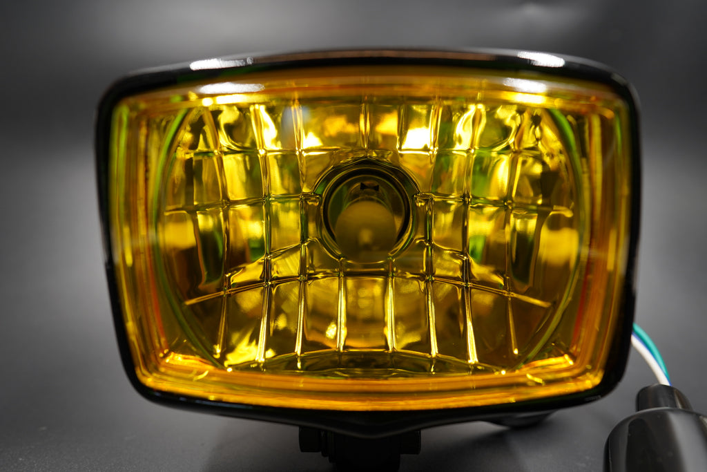 Front angle showing yellow lens glow and classic metal housing — ideal for café racers and custom bikes.